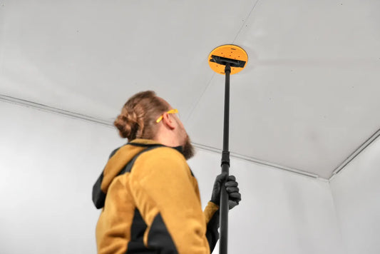 Handwerker schleift Zimmerdecke mit Mirka DecoSander 225 mm – ergonomischer Stielschleifer für staubfreies Schleifen von Gipskarton und Deckenflächen im Trockenbau.