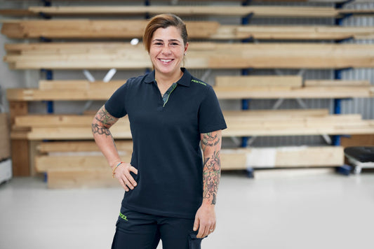 Festool Poloshirt Damen in Dunkelblau mit grünen Details, Frontansicht auf Modell in Werkstatt
