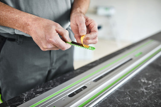 Festool Führungsschiene FS/2 mit grünem Gleitbelag wird von Hand positioniert auf Werkstück mit Maßstab