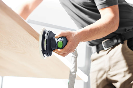Festool ETS EC 150/5 EQ Exzenterschleifer in Anwendung, grüner Start-Stopp-Schalter, Schleifteller auf Holzoberfläche