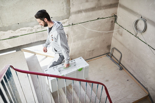 Festool Systainer³ SYS3 XXL 337 mit 64,2 Litern Stauraum auf Baustelle, Handwerker trägt Behälter die Treppe hinauf.