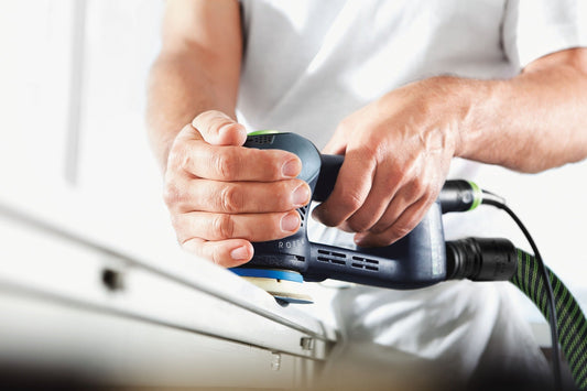 Festool Elektroschleifermaschine mit Schleifteller wird von Handwerkerhänden bedient, Klettbelag sichtbar.