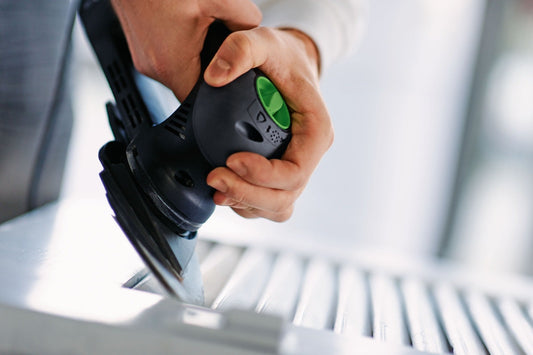 Festool Schleifer mit grünem Druckschalter in Hand über dreieckigen Schleifblättern Granat V93