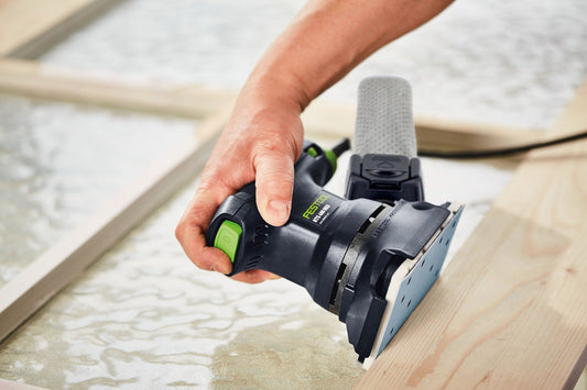 Festool Elektroschleifer mit grünem Schalter wird auf Holzoberfläche angewendet, Staubfangbeutel sichtbar.