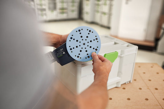 Festool Granat D150 Schleifscheibe mit 49-Loch-Absaugung in der Hand, hellblau, Systainer im Hintergrund