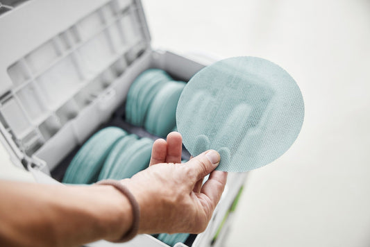 Festool Granat Net Schleifscheibe Ø 150 mm Körnung P120 in Hand vor geöffnetem Systainer³ mit sortierten Netzschleifscheiben