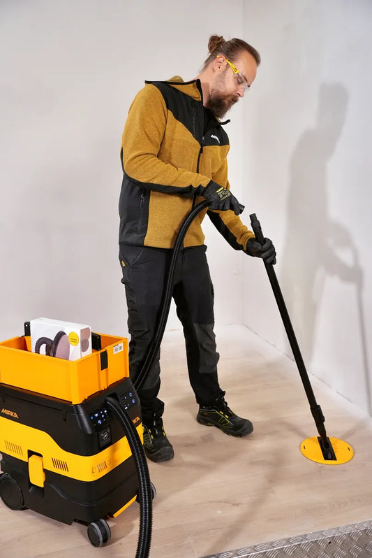 Handwerker schleift Boden mit Mirka DecoSander 225 mm und angeschlossenem Industriesauger – effizientes, staubfreies Schleifen für professionelle Oberflächenbearbeitung im Innenbereich.