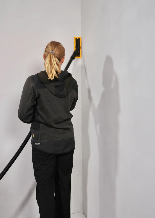 Frau schleift Wand mit Mirka DecoSander 80x230 mm – ergonomisches Schleifwerkzeug mit Absaugung für staubfreies Arbeiten an senkrechten Flächen im Innenausbau.